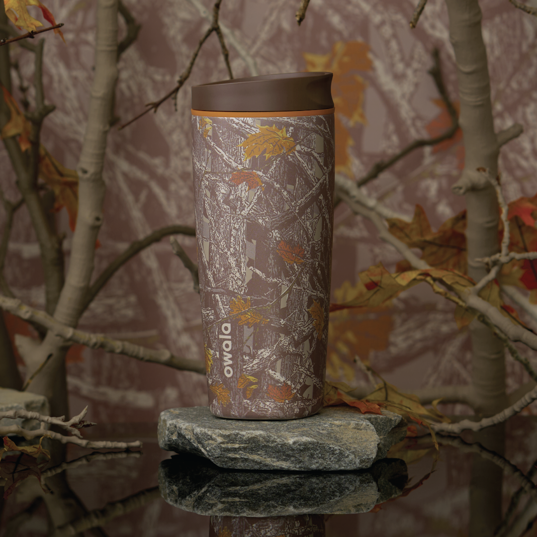 Owala FreeSip Sway in Out of Sight, woodland camo patterned body in brown and tan with matching brown flip cap and carry loop, shown on a mossy rock against a forest backdrop